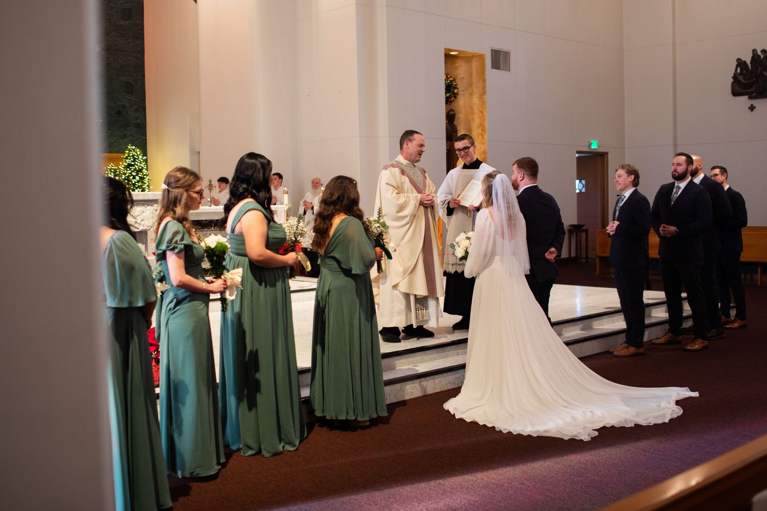 A wedding ceremony processional in a church with bridesmaids in green dresses walking down the aisle.