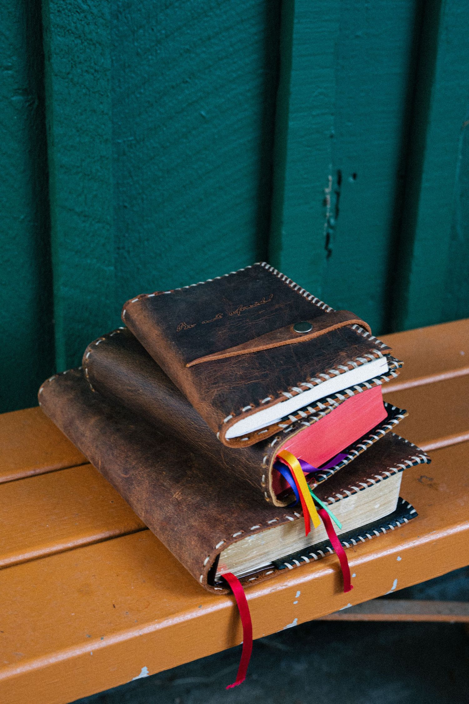 Brown leather book cover with colorful ribbons and spiral binding shown in various angles on wooden bench surface.