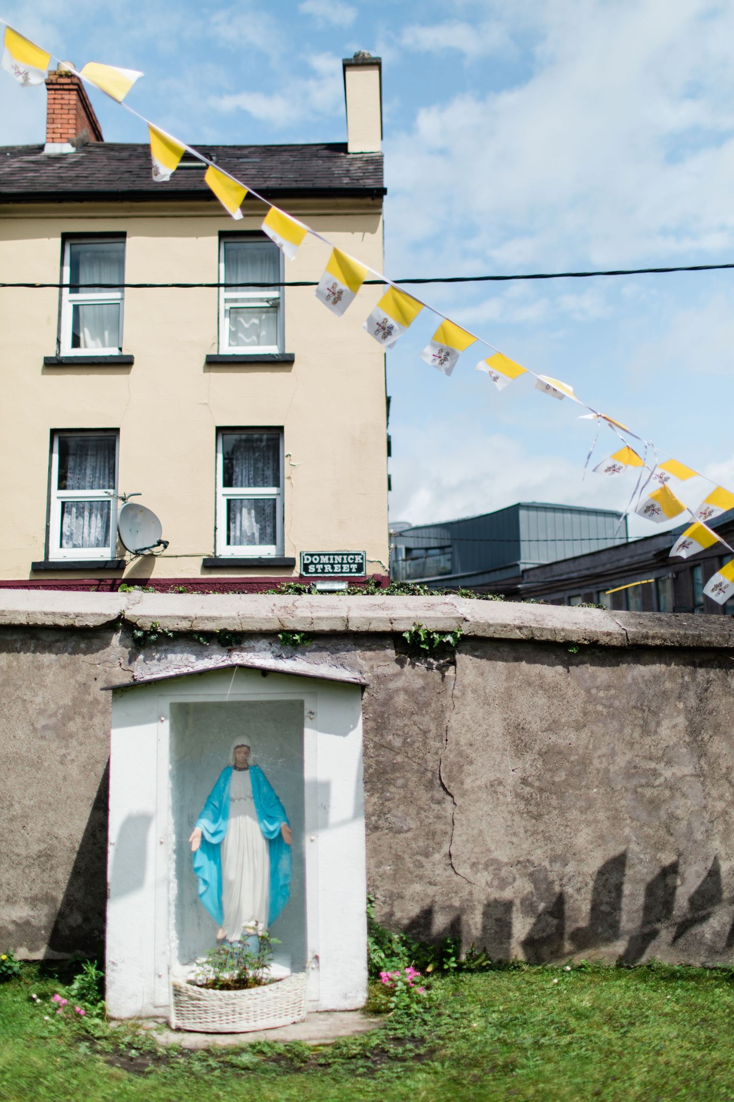 Statue of the Virgin Mary in a roadside shrine decorated with yellow and white papal bunting.