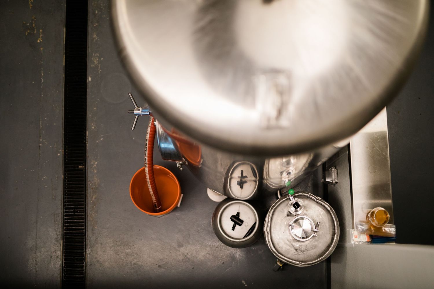 Stainless steel beer fermentation tanks in a brewery with a dark background and dramatic lighting.