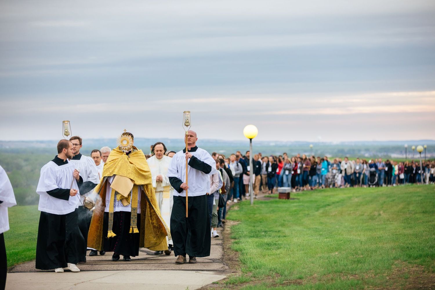 Wedding party walks across green hilltop meadow during golden hour with scenic mountain views in background.