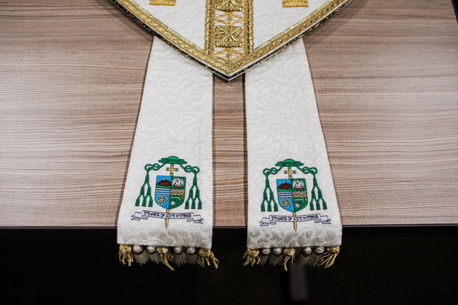 Ornate white and gold Catholic bishop vestment stole embroidered with green heraldic coat of arms symbols.