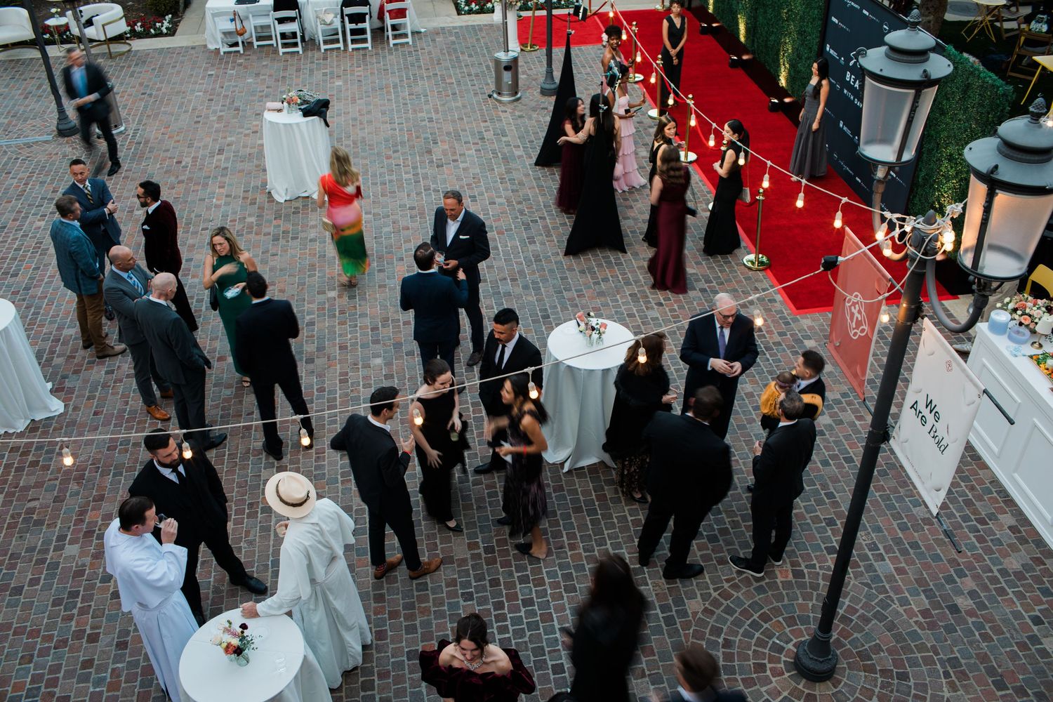 Guests mingle and socialize during an outdoor cocktail reception on a brick patio with red and white decor.