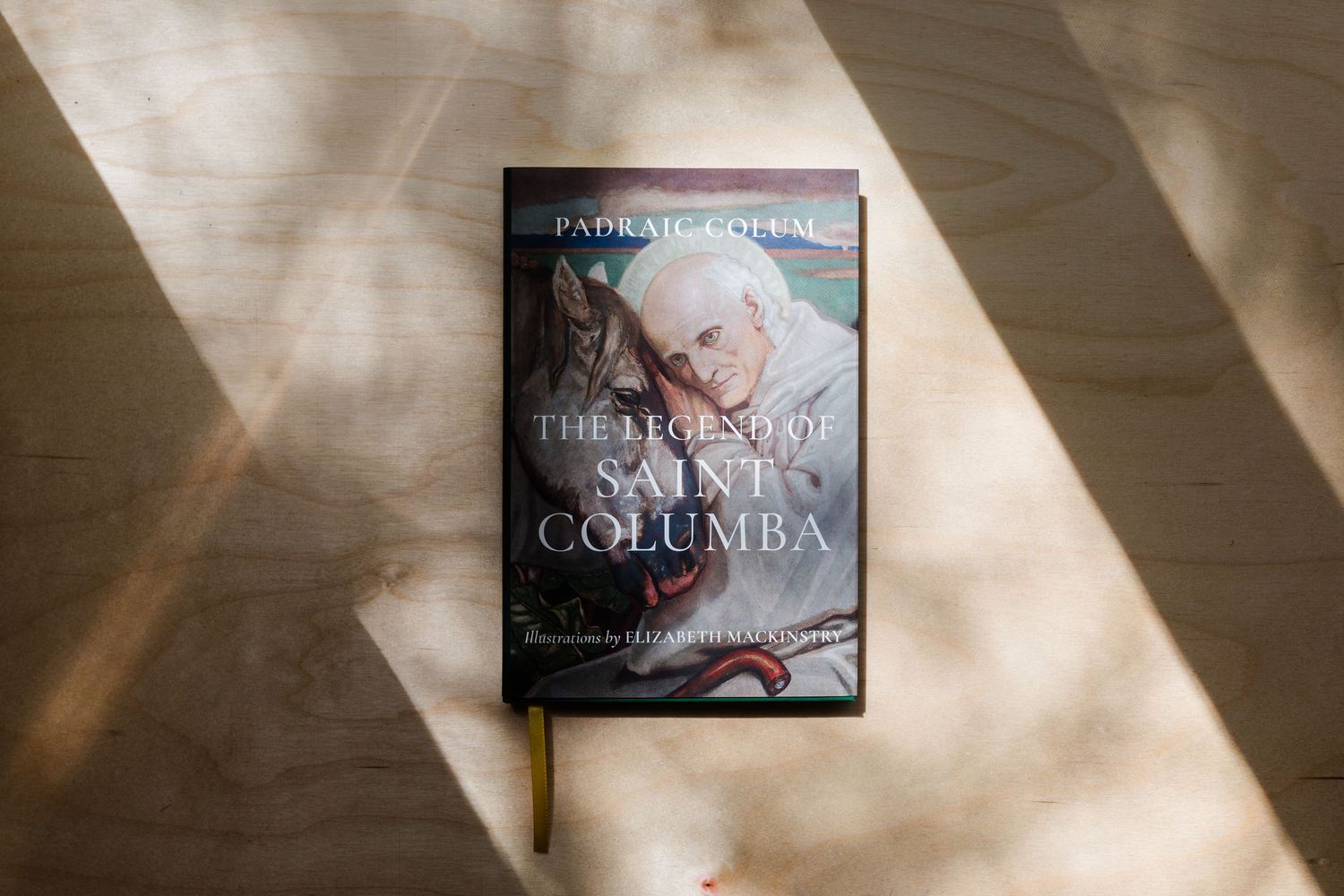 Book 'The Legend of Saint Columba' by Padraig Colum resting on a wooden surface in natural light.