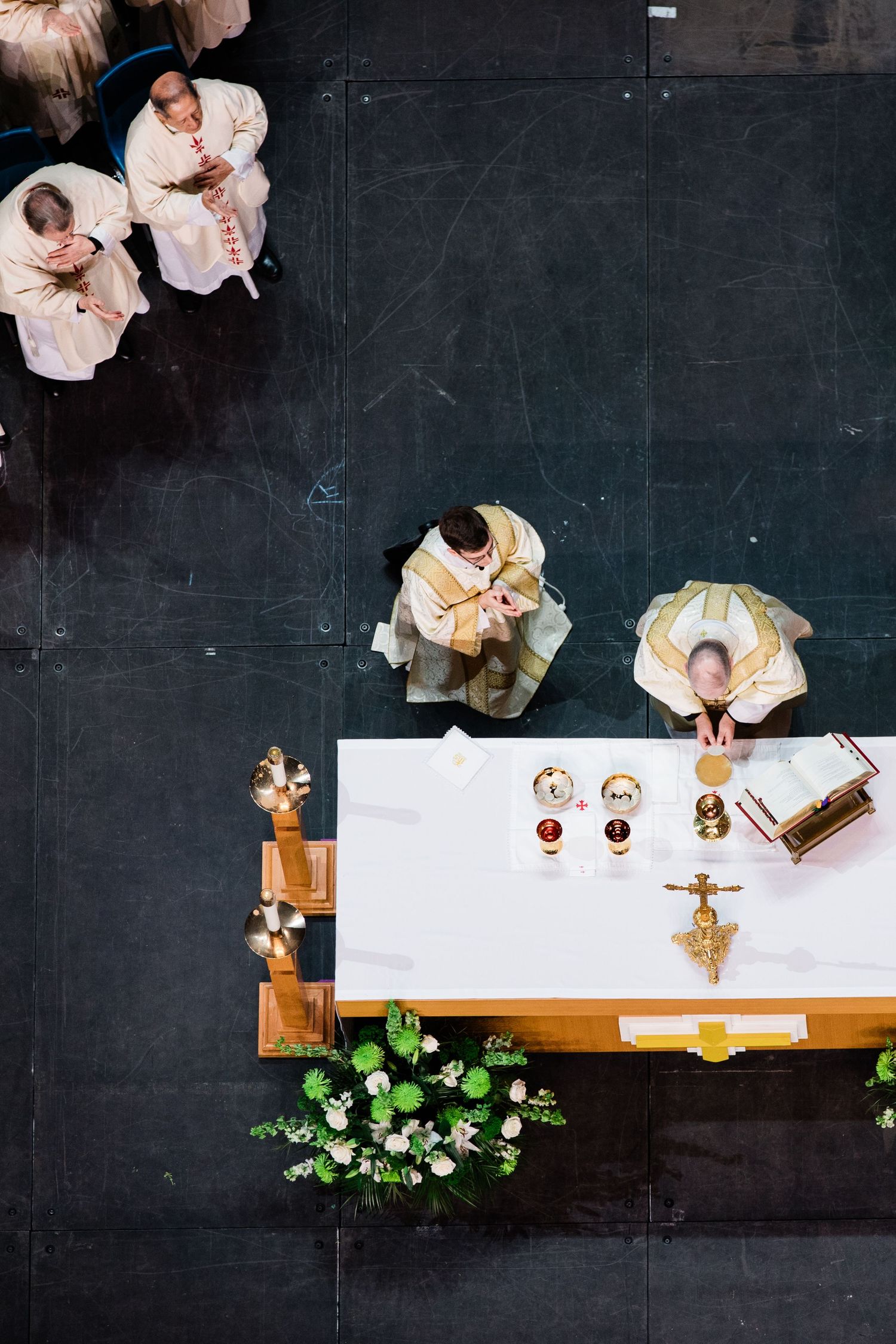Overhead view of an altar during Catholic mass with priests and floral decorations.