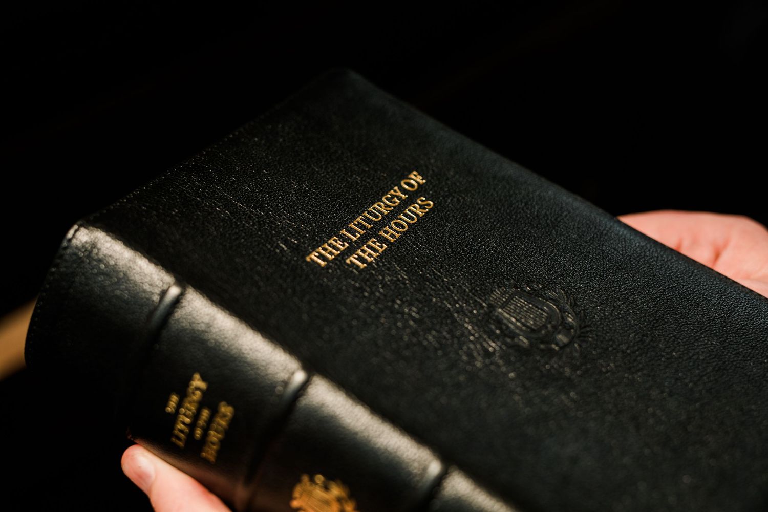 Black leather Liturgy of the Hours book spine with gold embossed lettering held in hand.