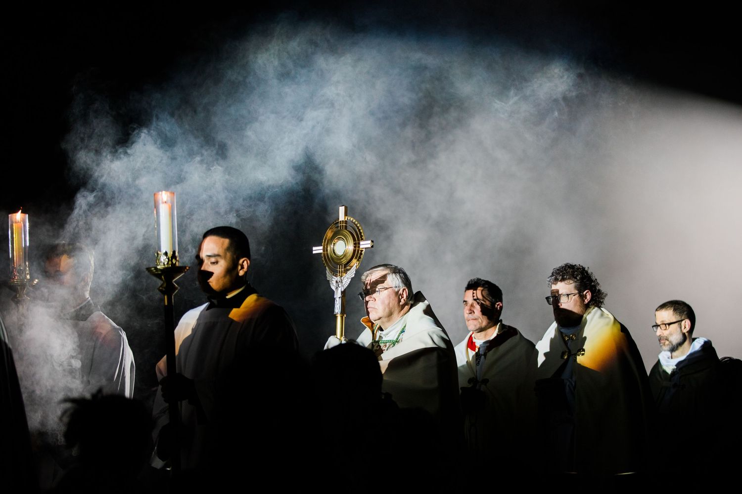 A group of people standing in a line with smoke surrounding them in a dark atmospheric setting.