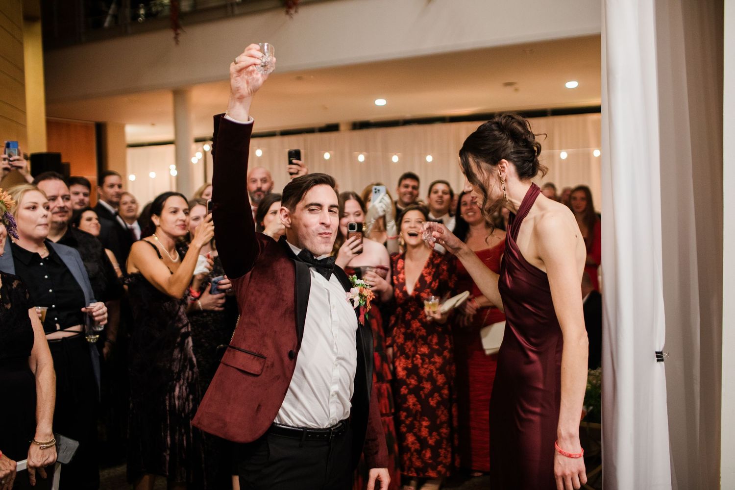 Wedding guests dancing and celebrating together in a reception hall with ambient lighting.