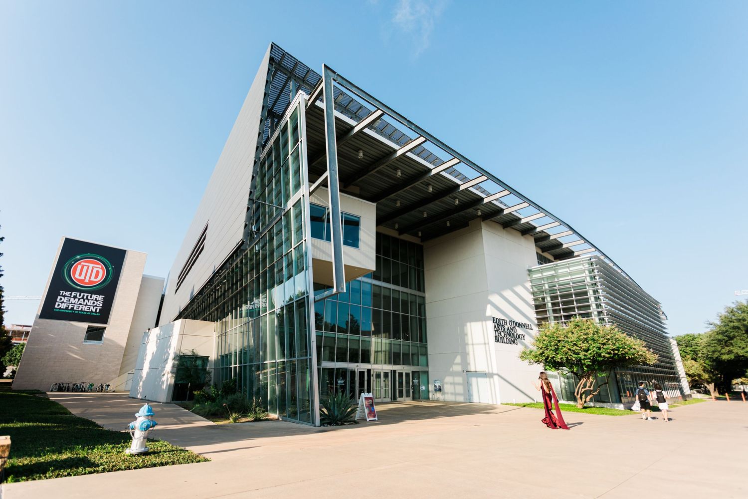 Modern glass and steel building exterior with angular architecture and curved walkway under bright blue sky.
