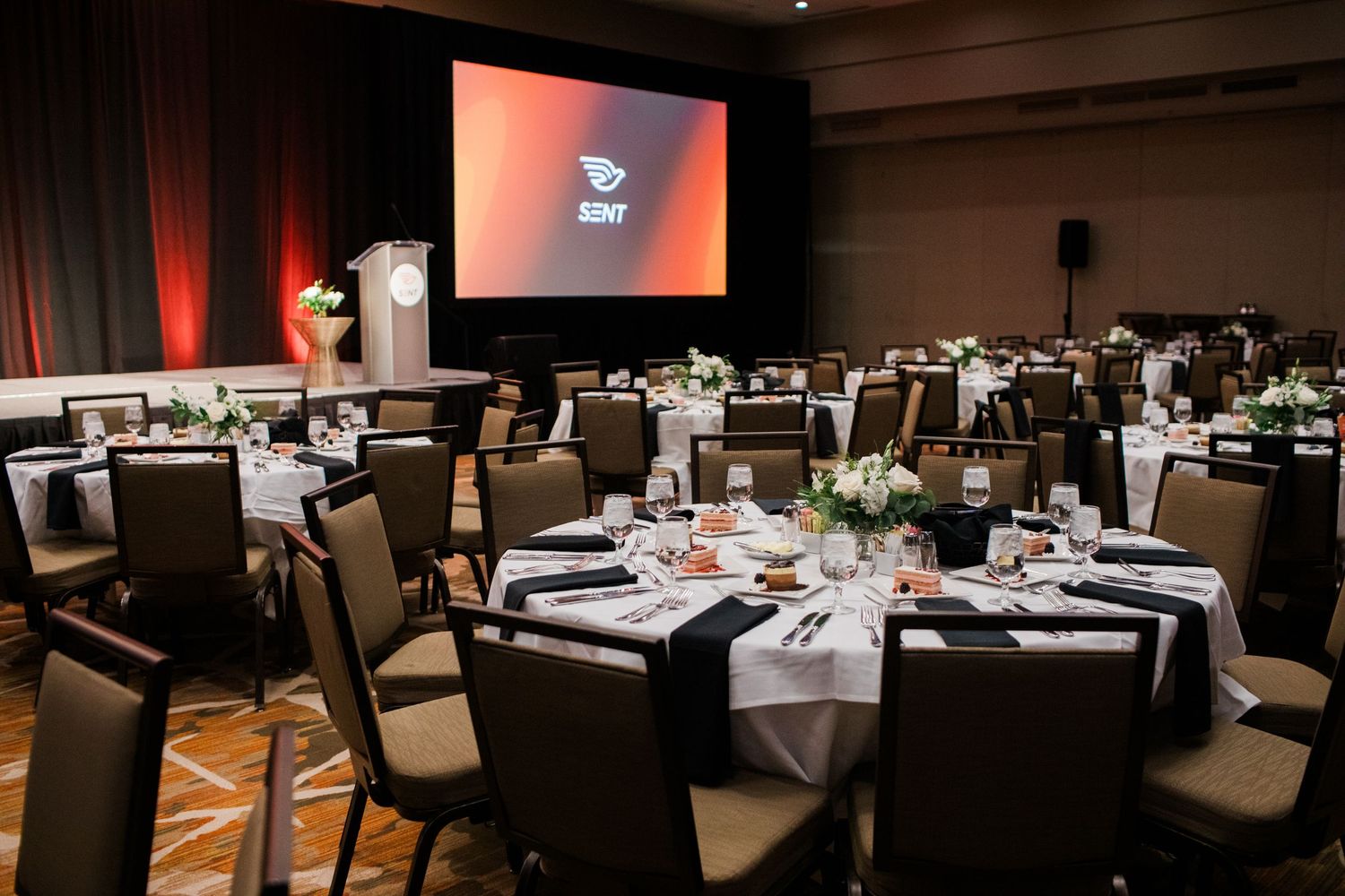 Elegant SUNY banquet hall with round tables, white linens, floral centerpieces, and a large projection screen.