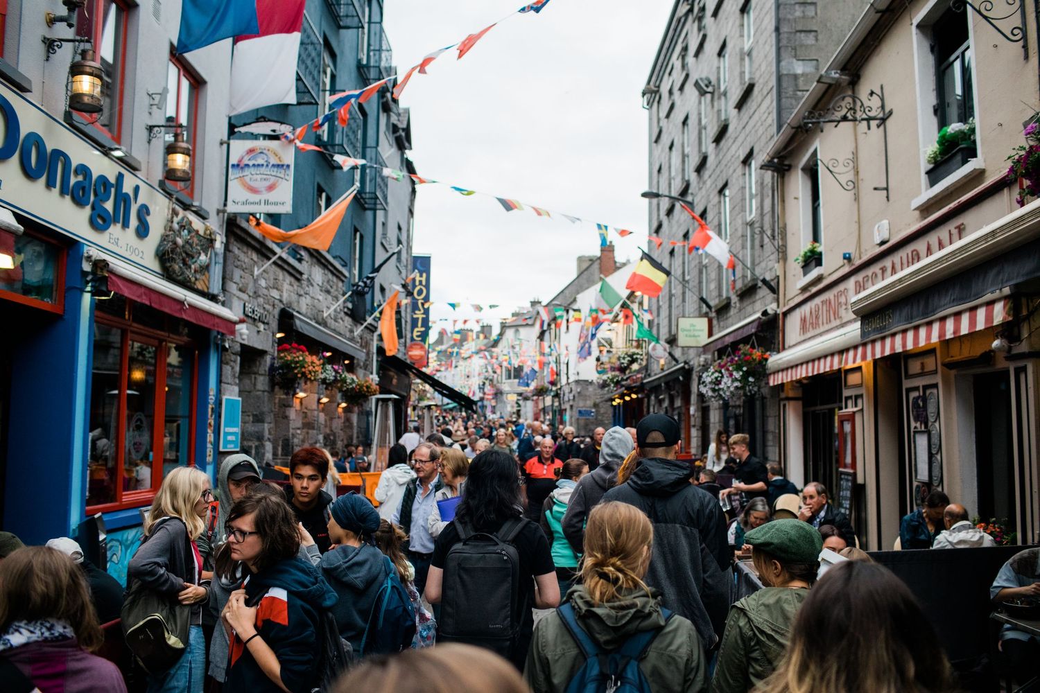 Crowds of tourists and locals filling a busy colorful shopping street in Galway, Ireland.