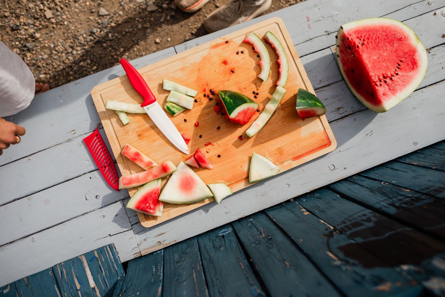 Fresh watermelon slices arranged on a gray wooden picnic table surface.