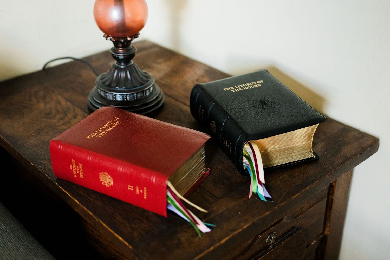 Two holy bibles with colorful bookmarks on a wooden side table next to a vintage lamp.