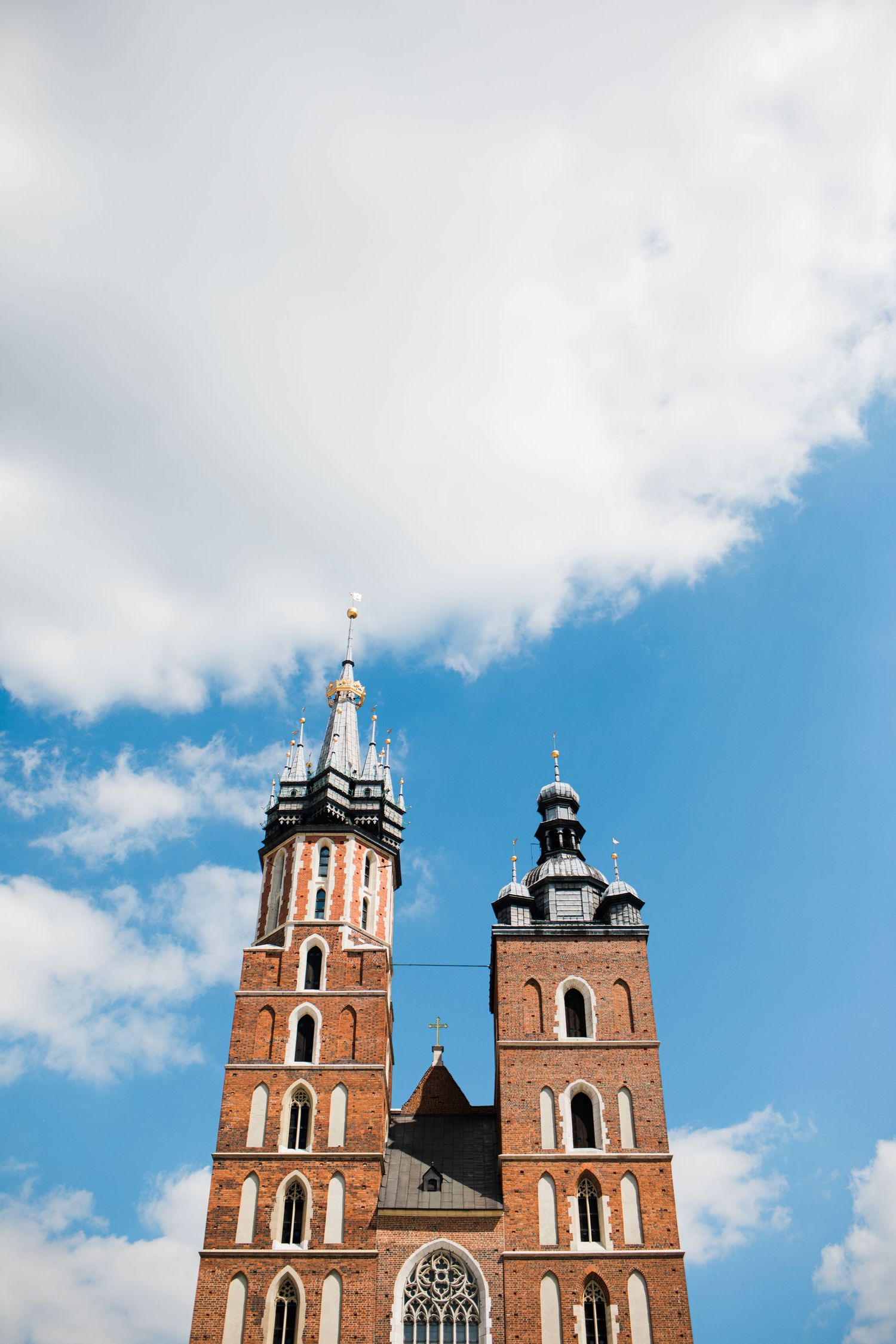 Twin brick towers of St. Mary's Basilica in Krakow against a blue cloudy sky.