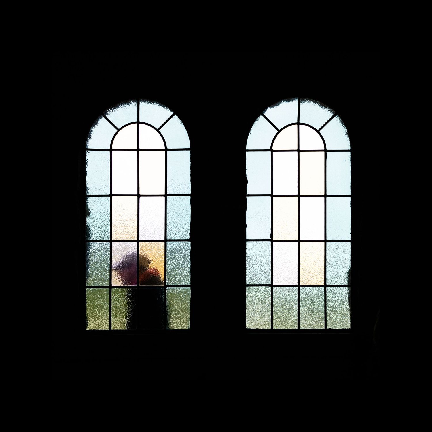 Two arched windows with sunlight streaming through create a silhouette effect against a dark background.