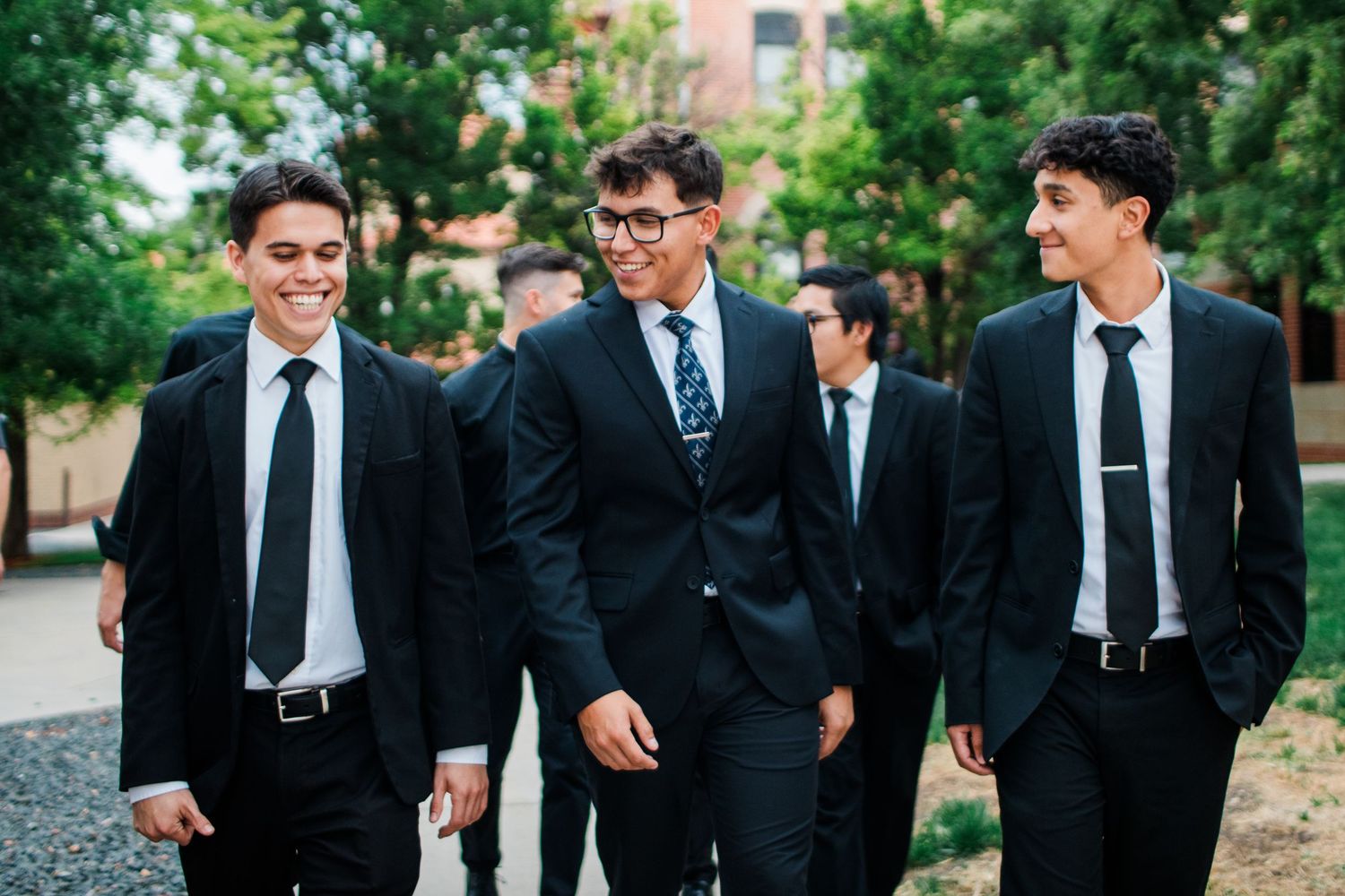 Groomsmen in black suits and ties share candid moments and laughter during outdoor wedding photos.