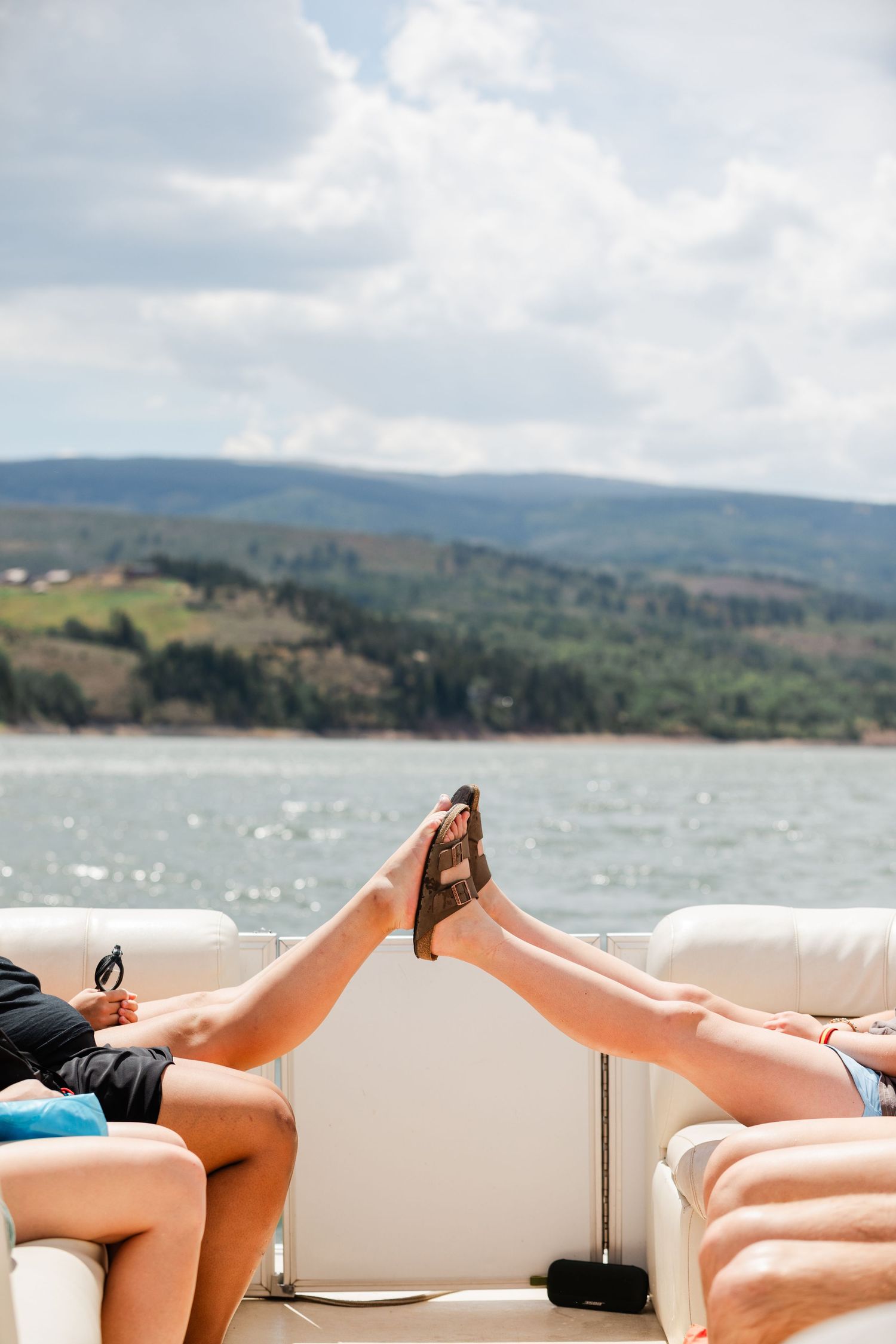 People relaxing on lounge chairs overlooking a scenic mountain lake on a sunny day.