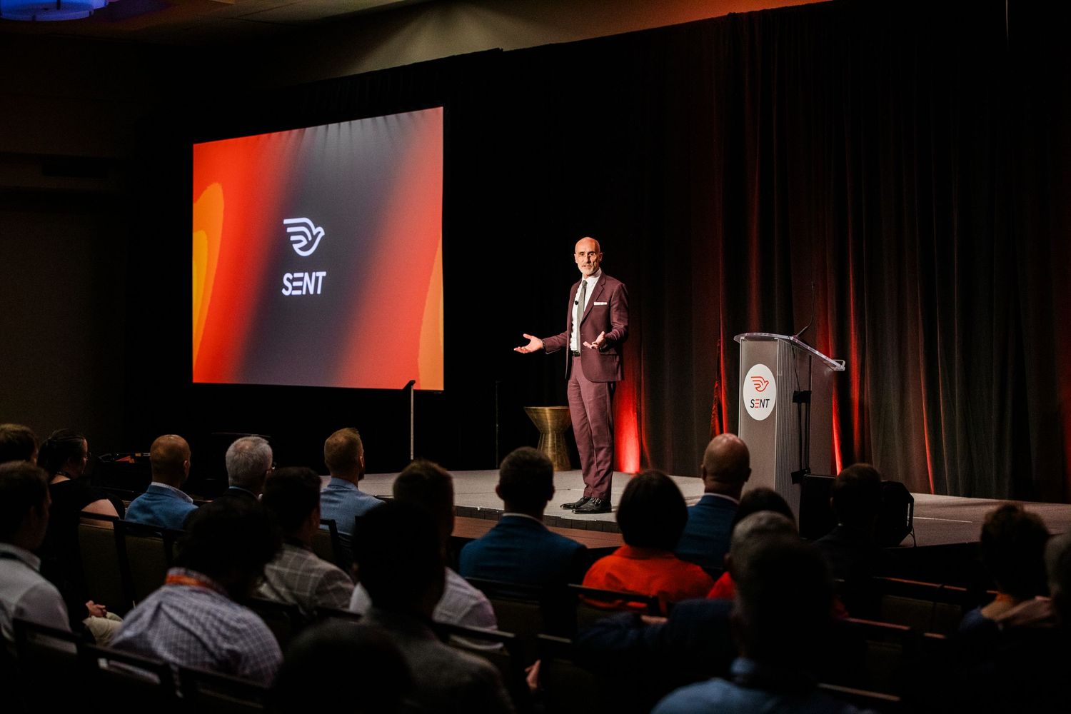 A speaker presents on stage at the Sent Summit conference with a branded screen backdrop.
