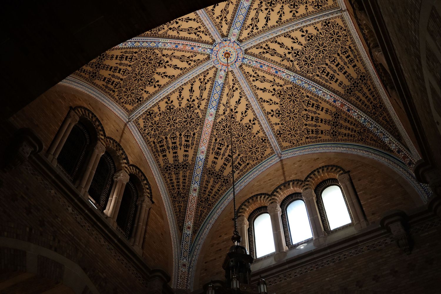 Ornate vaulted cathedral ceiling with intricate golden details and arched windows letting in natural light.