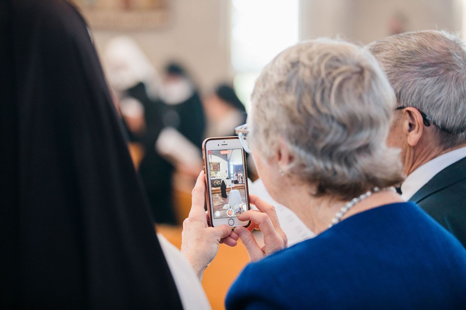 Elderly couple viewing wedding photos on a smartphone during a church ceremony.