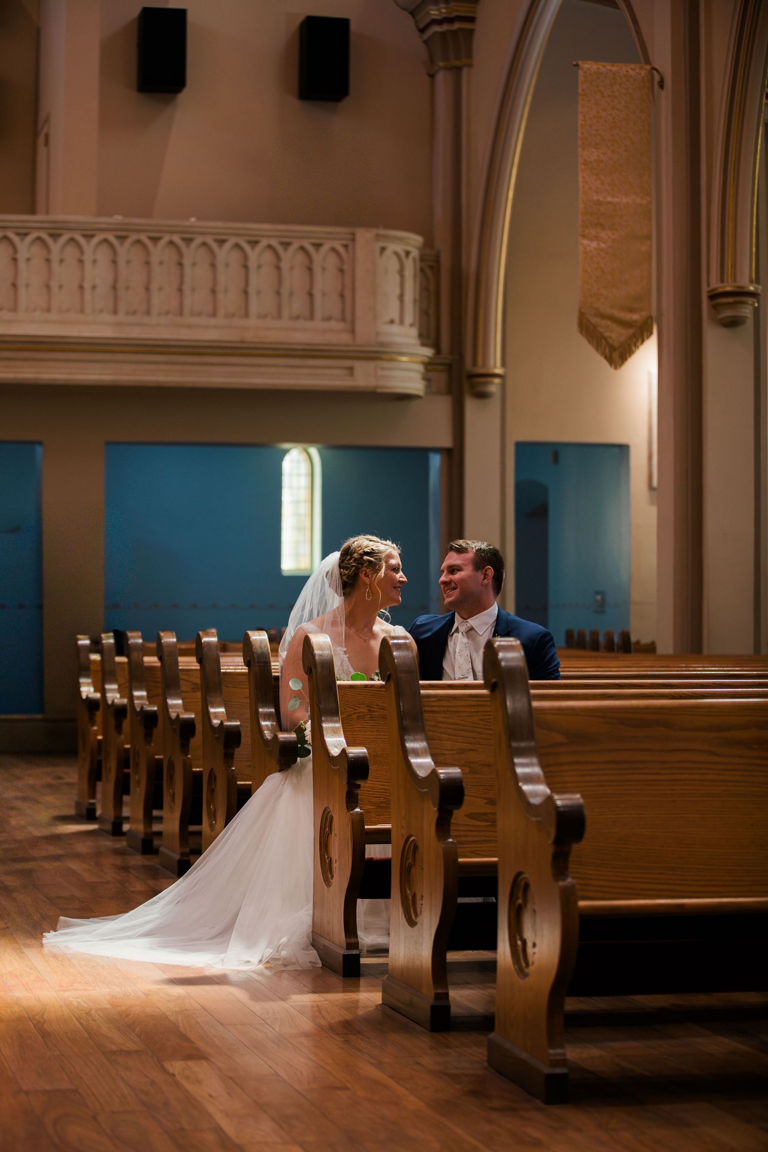 Bride and groom sitting together in wooden church pews after wedding ceremony.