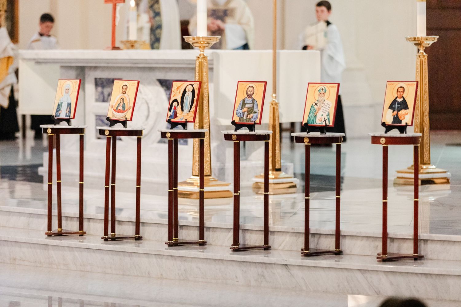 Orthodox icons displayed on wooden easels inside a church during a religious ceremony with clergy in background.