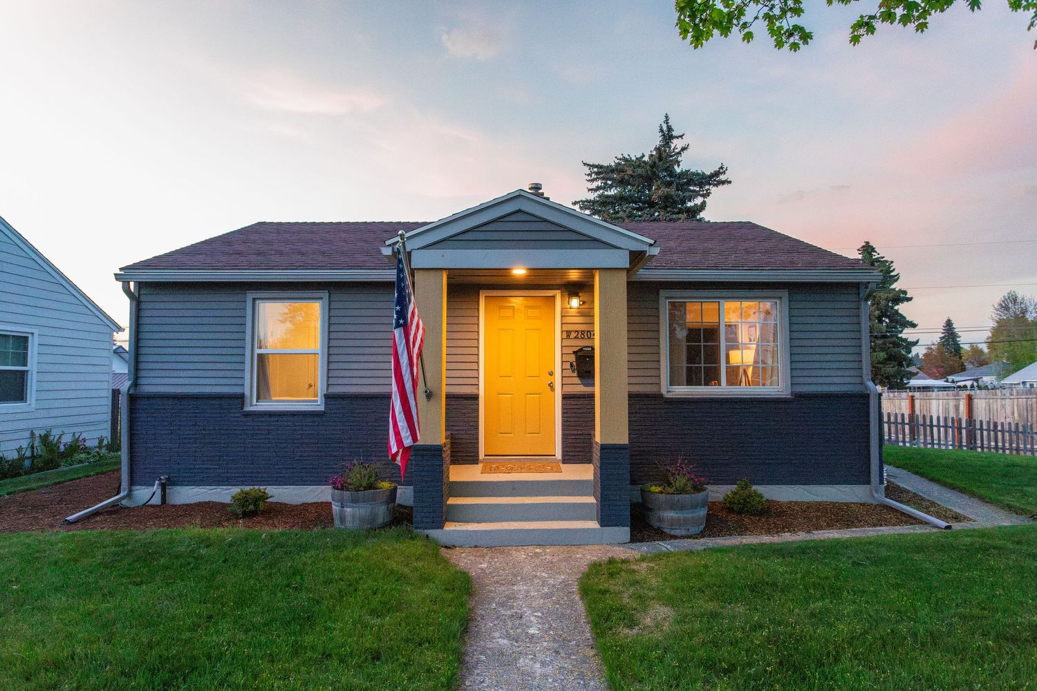 Exterior views of modern ranch-style homes at dusk with glowing windows and American flags displayed.