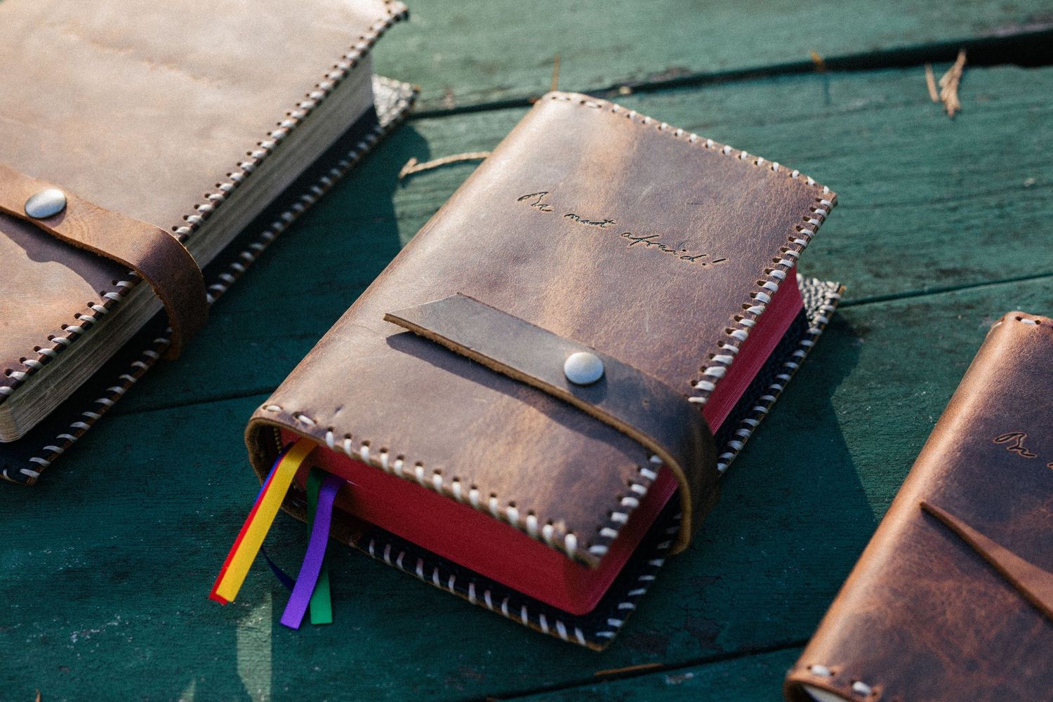 Handcrafted brown leather journal notebook with colorful bookmark ribbons on a teal wooden surface.