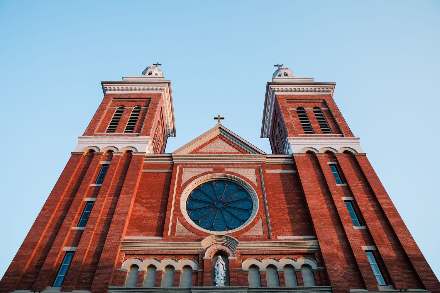 Red brick Gothic church spires with ornate architectural details against a bright blue sky.