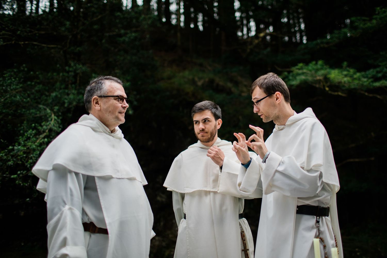 Group in white ceremonial robes gathered outside in a wooded setting during a formal occasion.