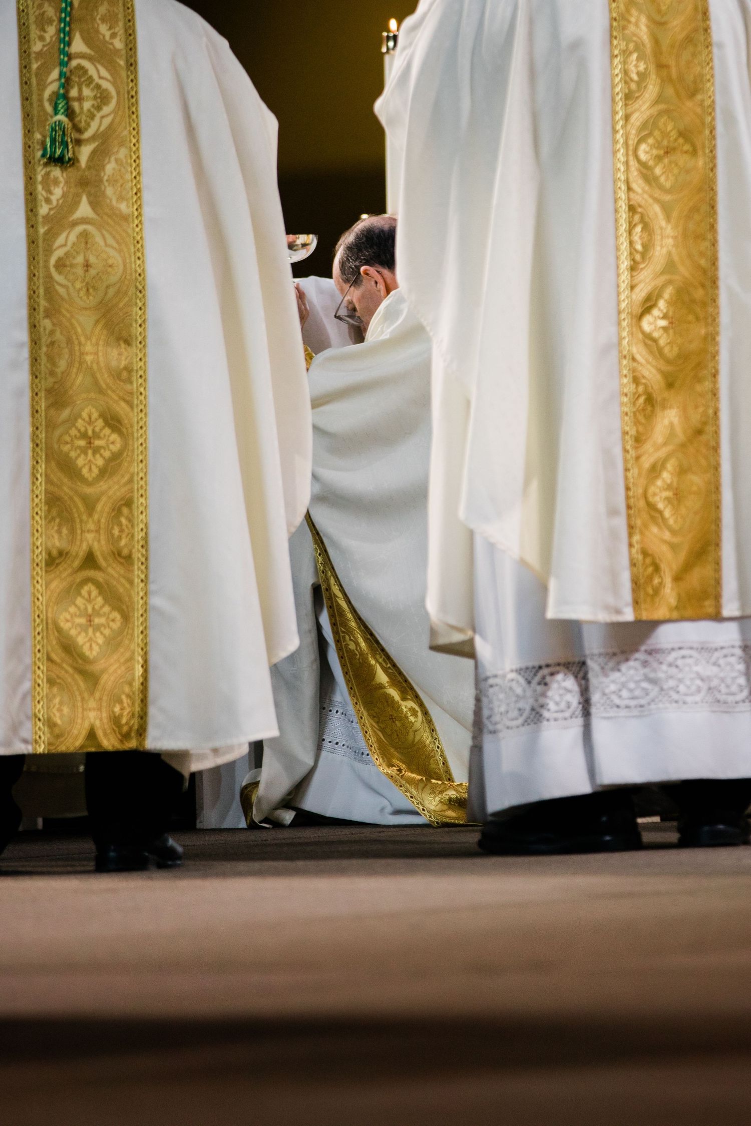 White-robed clergy members stand in a row against ornate gold-trimmed walls during a religious ceremony.