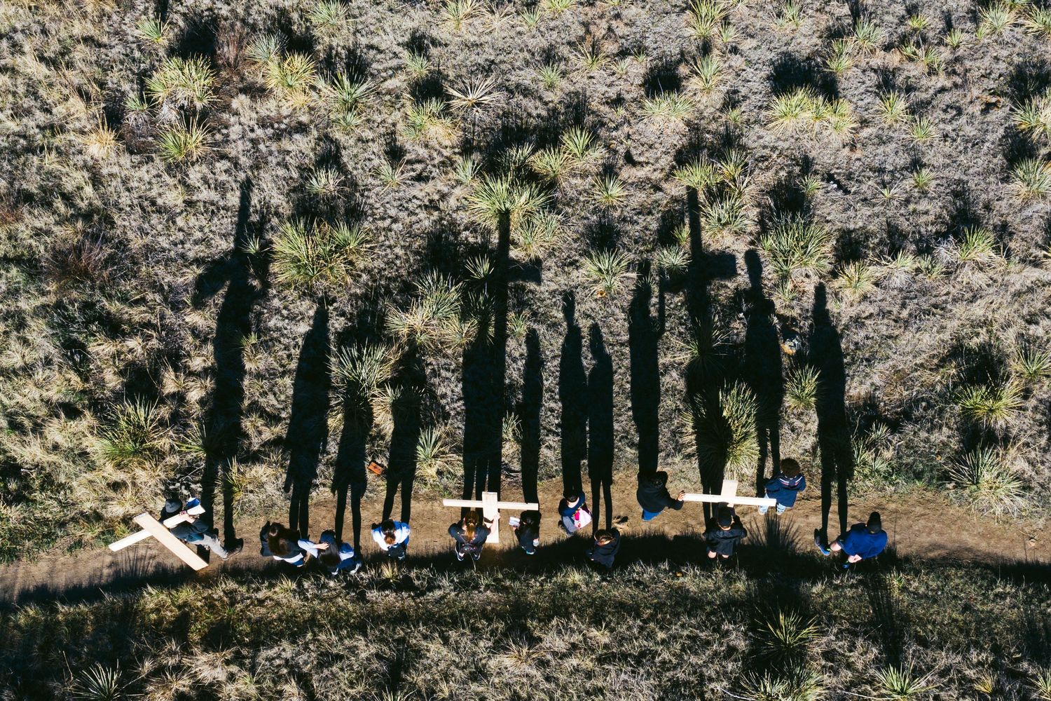 A silhouette of a group of people hiking on a rocky mountainside trail against a bright sunny background.