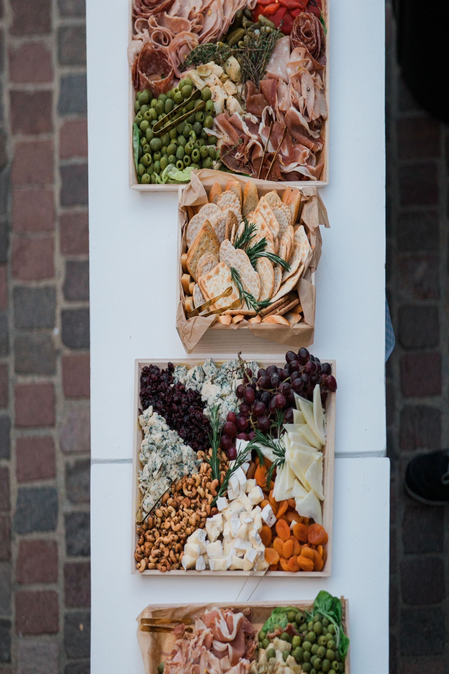 Overhead view of charcuterie boards arranged vertically featuring meats, cheeses, fruits and nuts in wooden boxes.