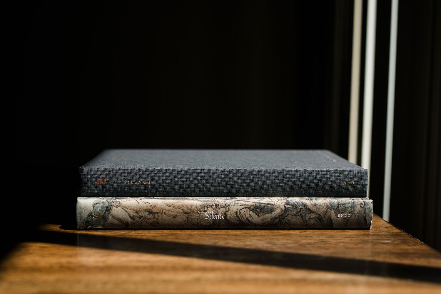 Two stacked hardcover books on a wooden surface, dramatically lit against a dark background.