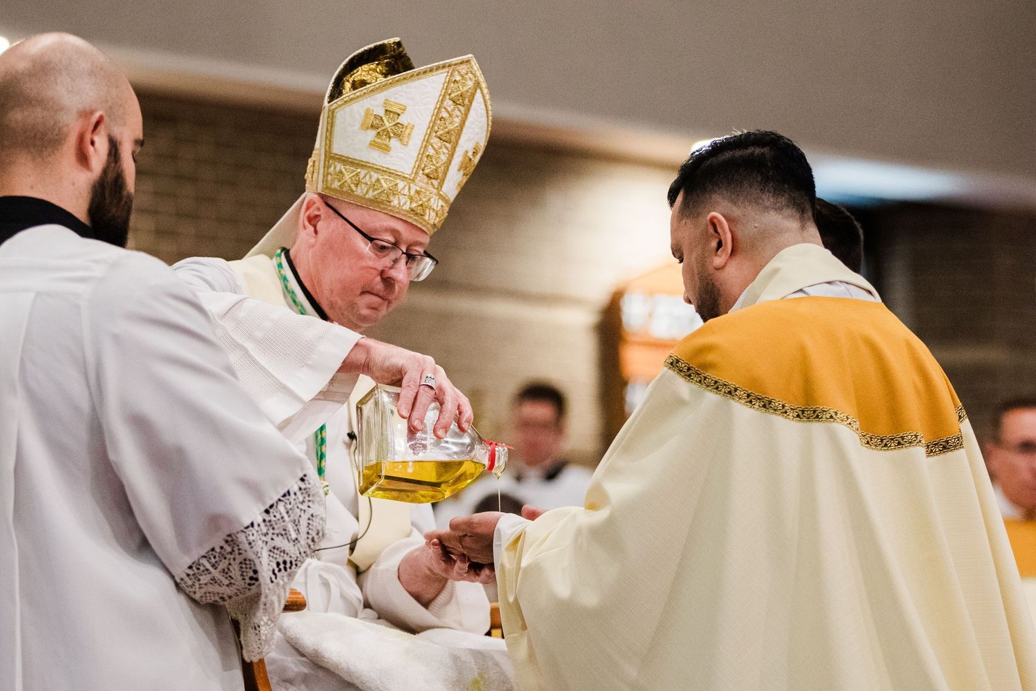 Bishop in ceremonial vestments performing a Catholic baptism rite, anointing an infant with holy oil during Mass.