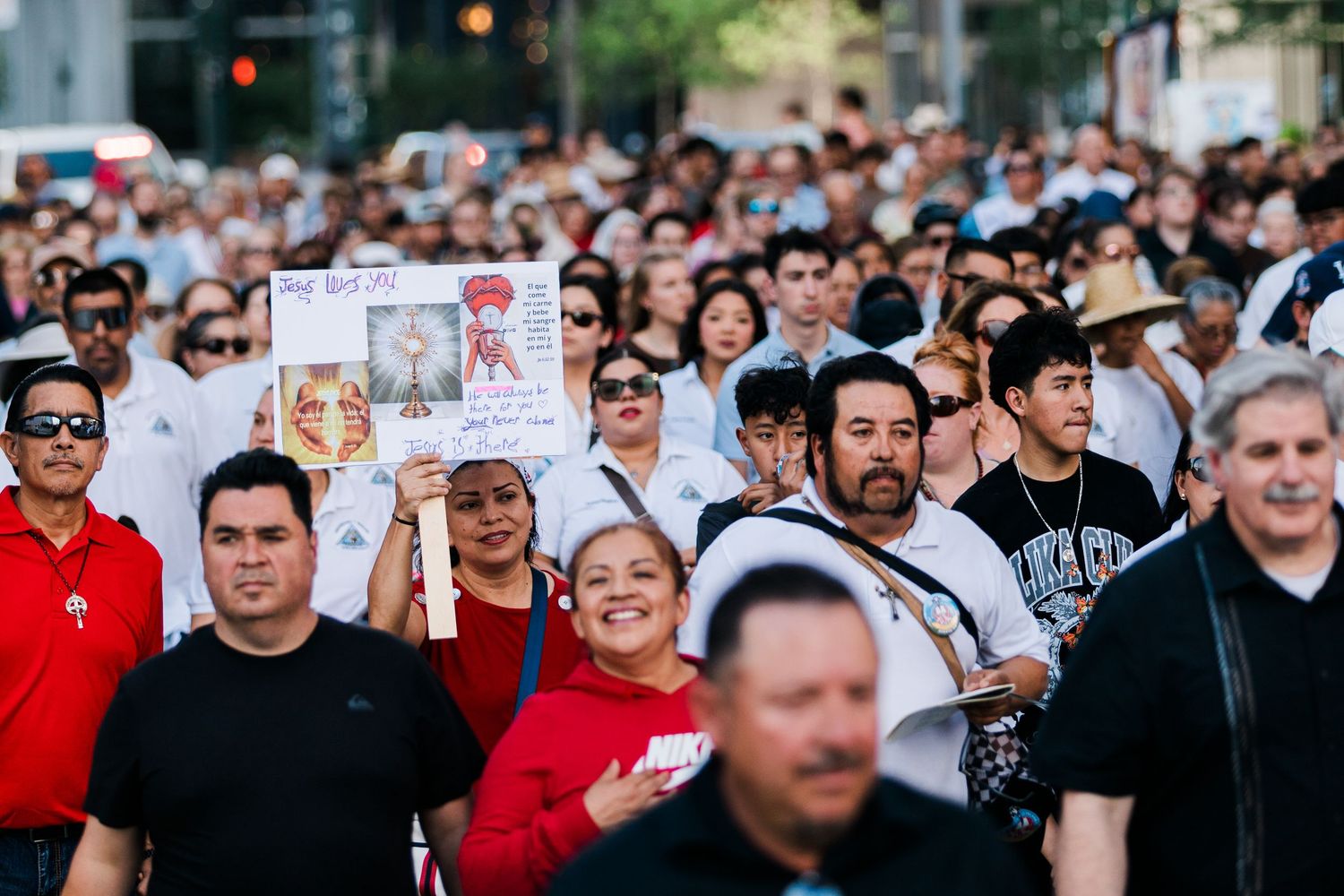 Large crowd marching in a street protest, with one participant holding a religious sign among diverse demonstrators.