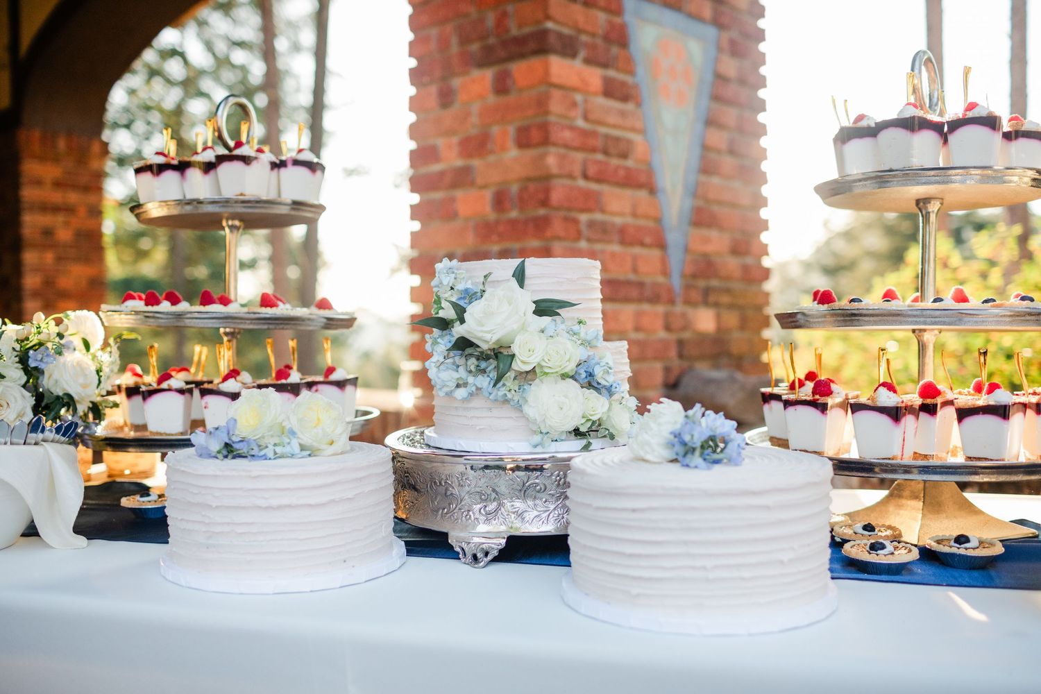 Elegant wedding dessert table featuring white tiered cakes adorned with blue hydrangeas and floral arrangements.