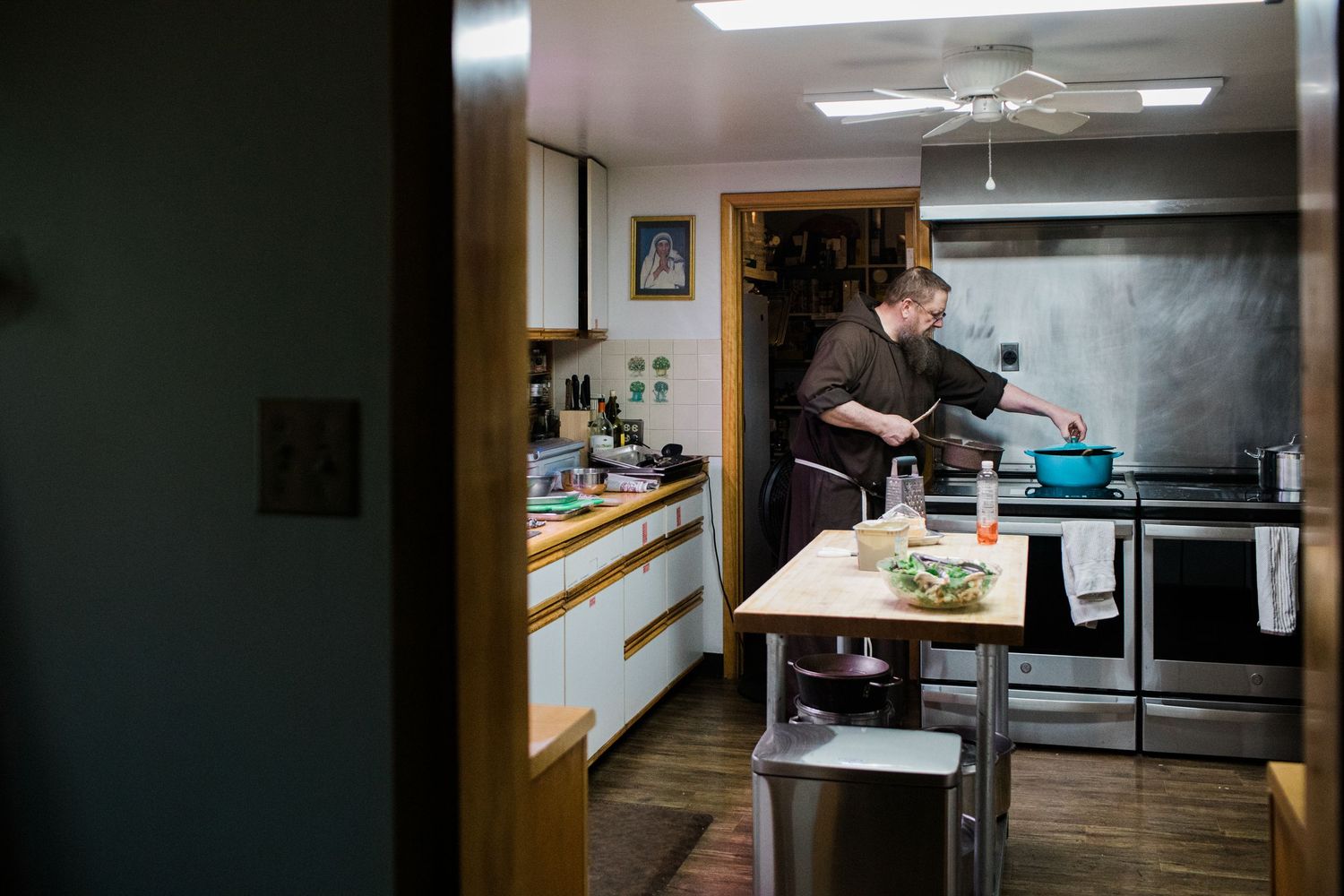 Person cooking in a modern kitchen, standing at an island counter with pots on the stove in a warmly lit home.