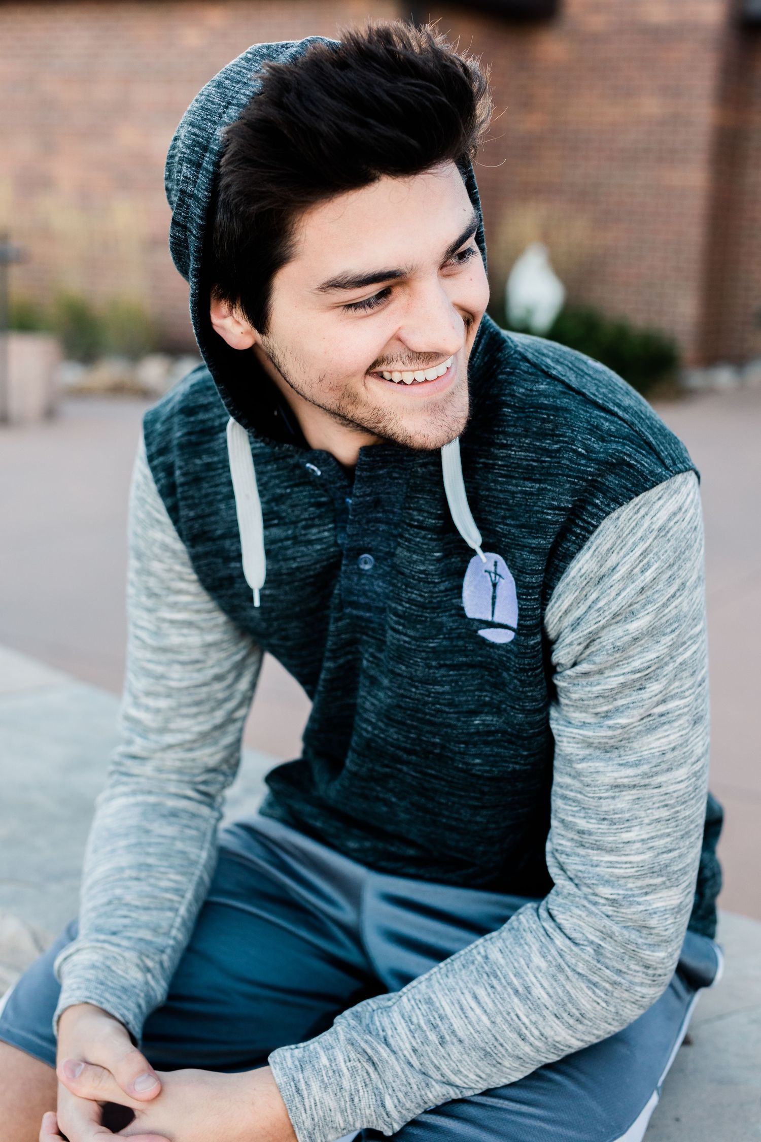 A candid outdoor portrait of someone wearing a teal beanie and two-toned sweater with a genuine smile.