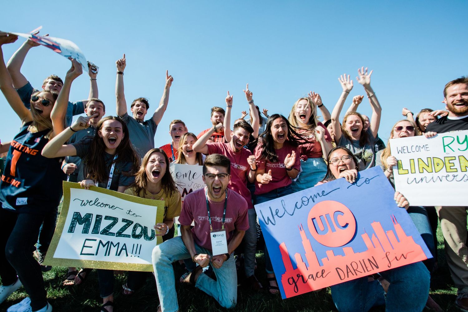 A large group of students holds up signs and cheers during an outdoor protest rally on a sunny day.