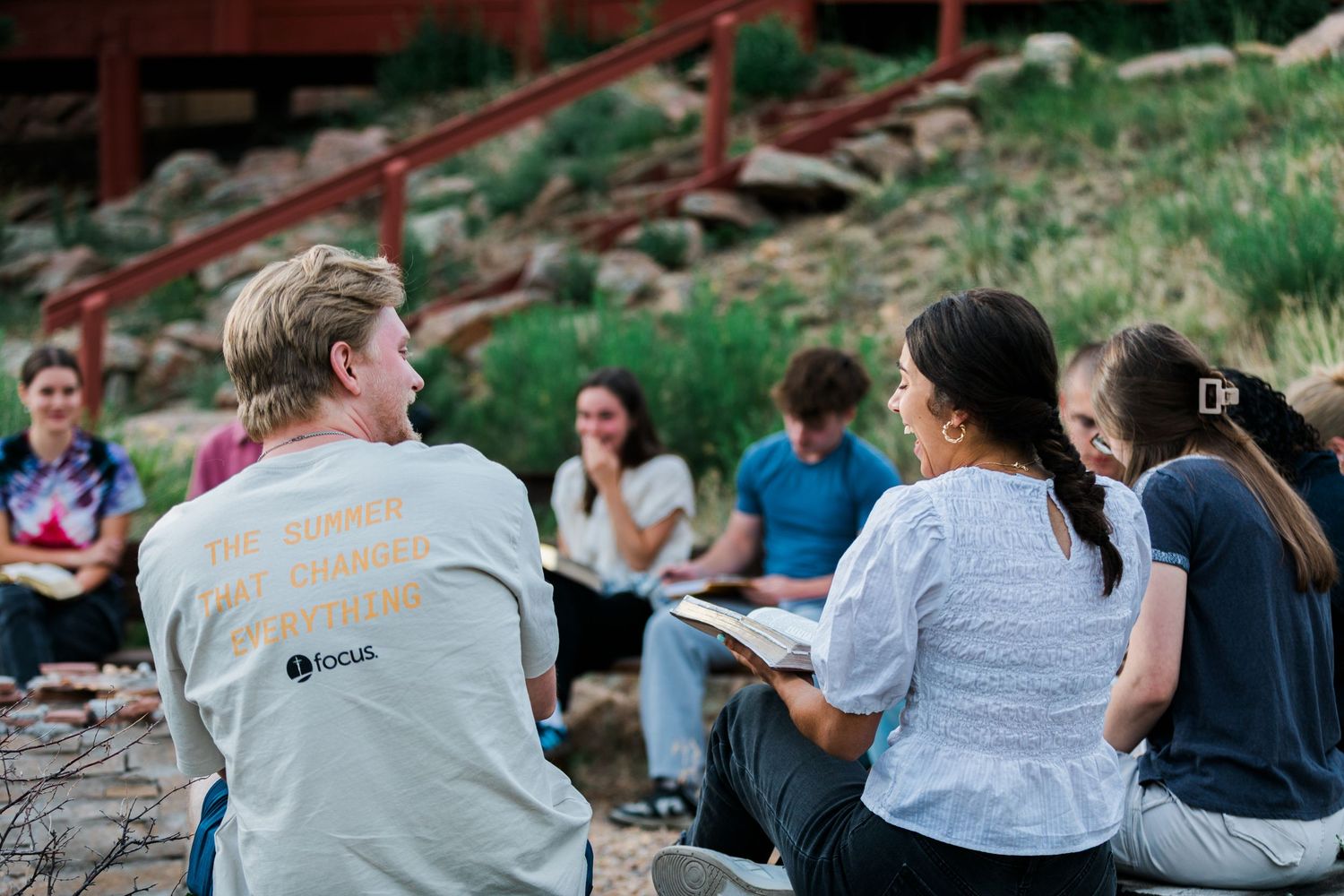 Students gather outdoors for a small group Bible study discussion at a Christian summer camp retreat.
