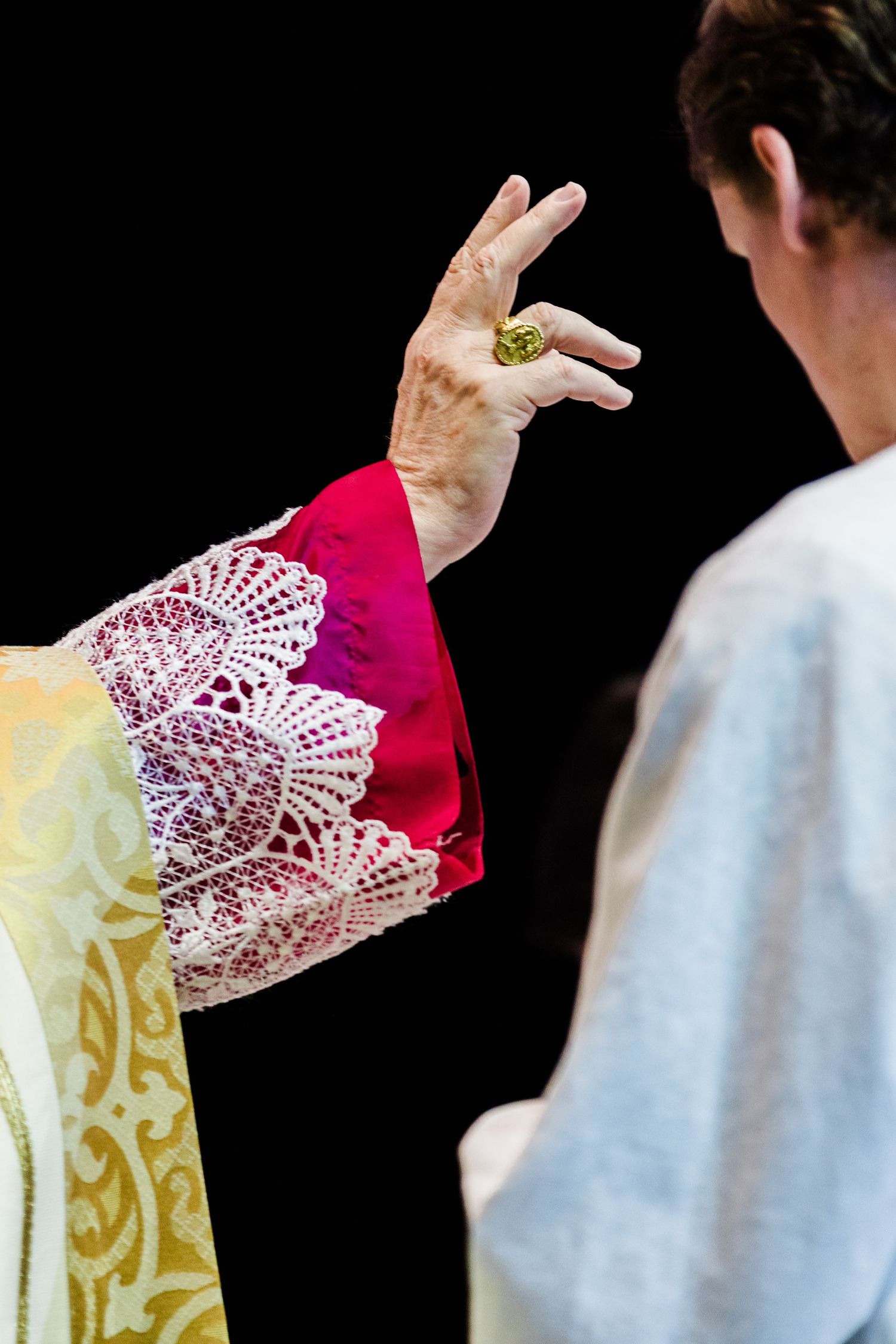 Close-up of ornate white lace and red religious vestments against a dark background.