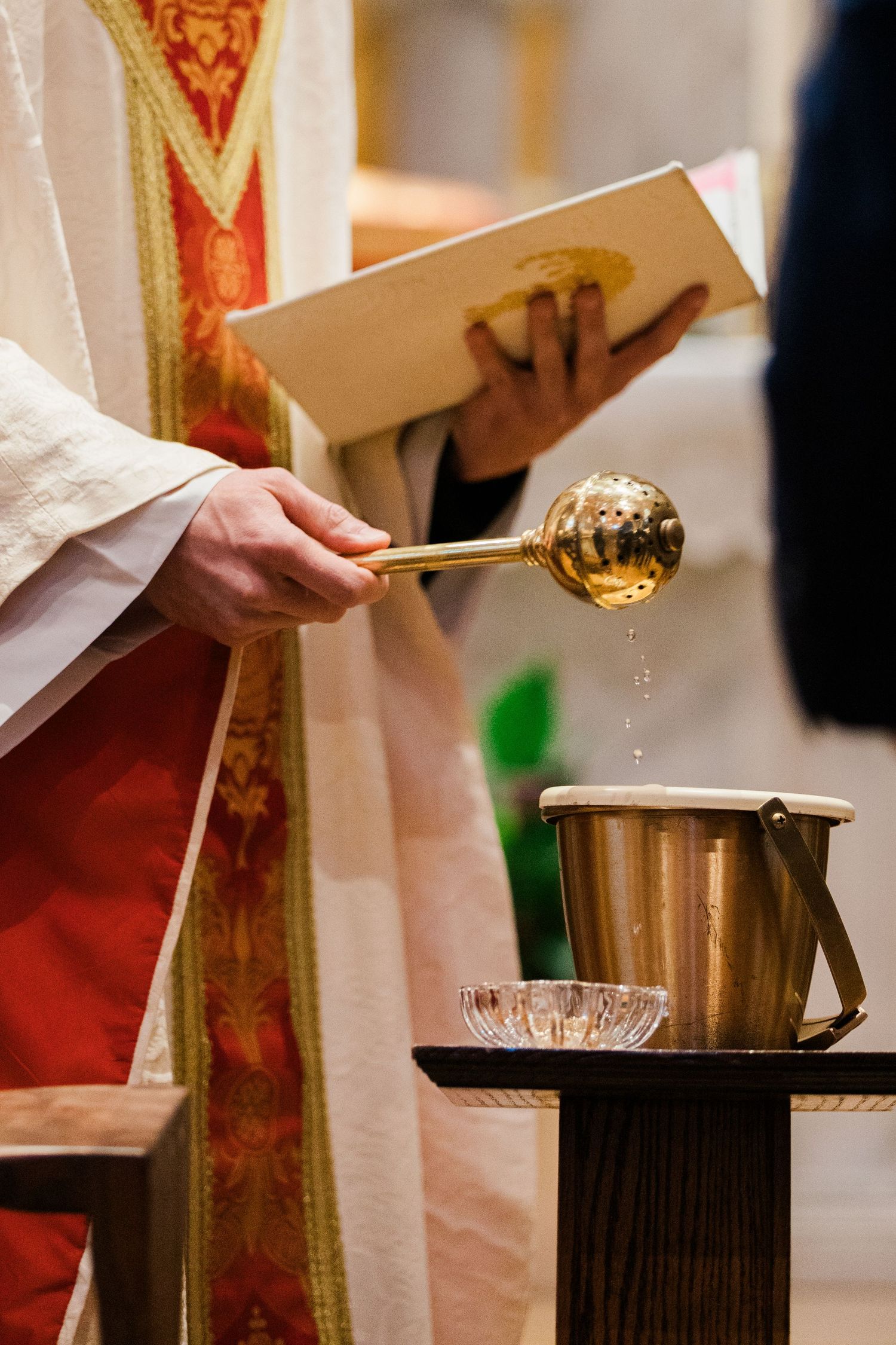Catholic priest blessing holy water with golden ladle during a wedding ceremony in church.