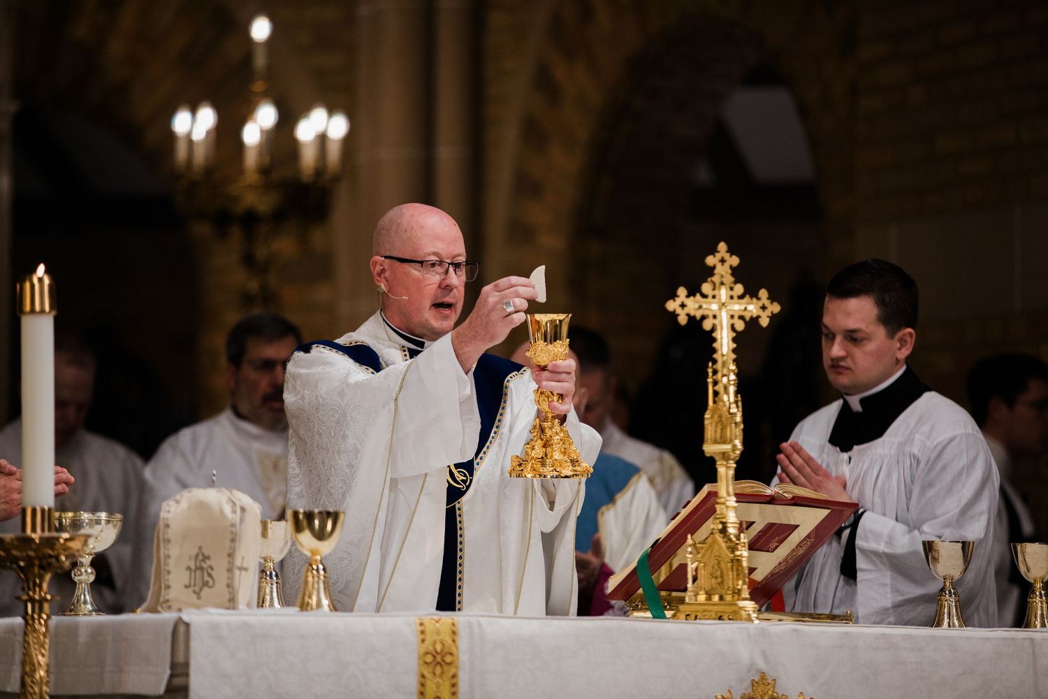 Catholic priest elevates golden chalice at ornate altar during solemn Mass ceremony.