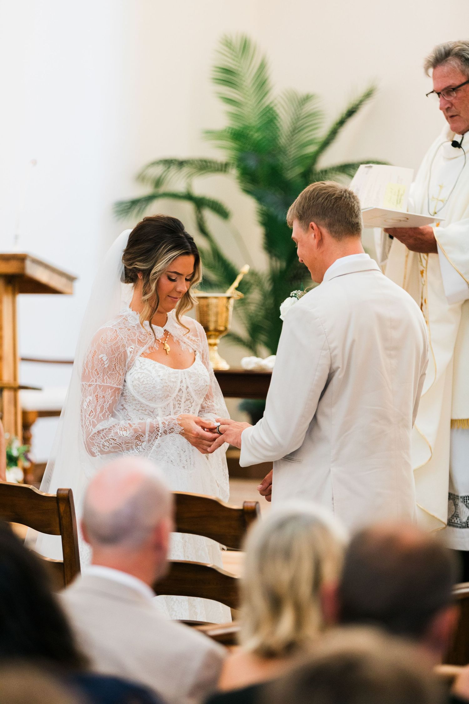 Bride and groom exchange rings at the altar during a church wedding ceremony with a priest officiating.