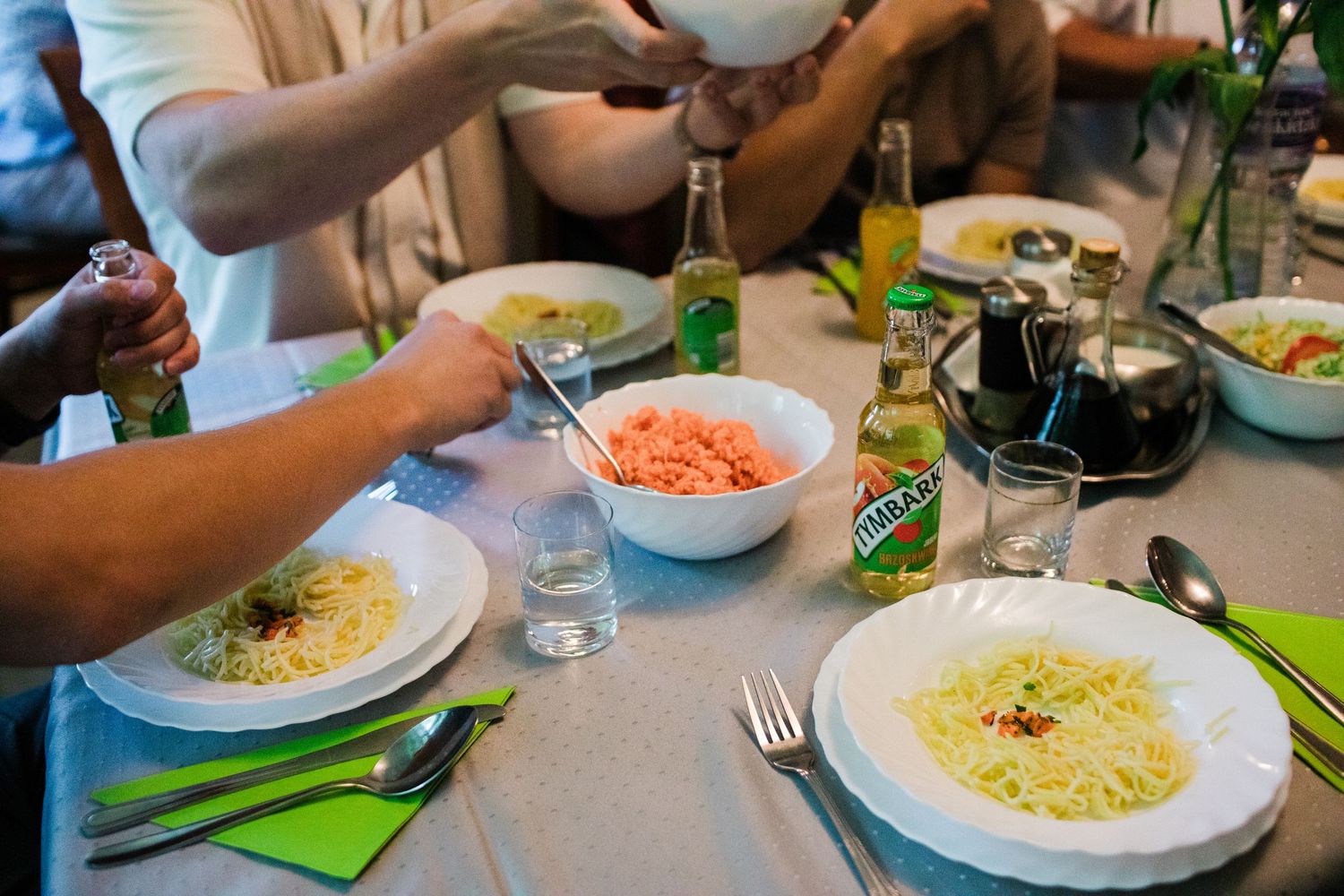 Group dining at a restaurant table with plates of spaghetti, Birell bottles, and fresh salad bowls.