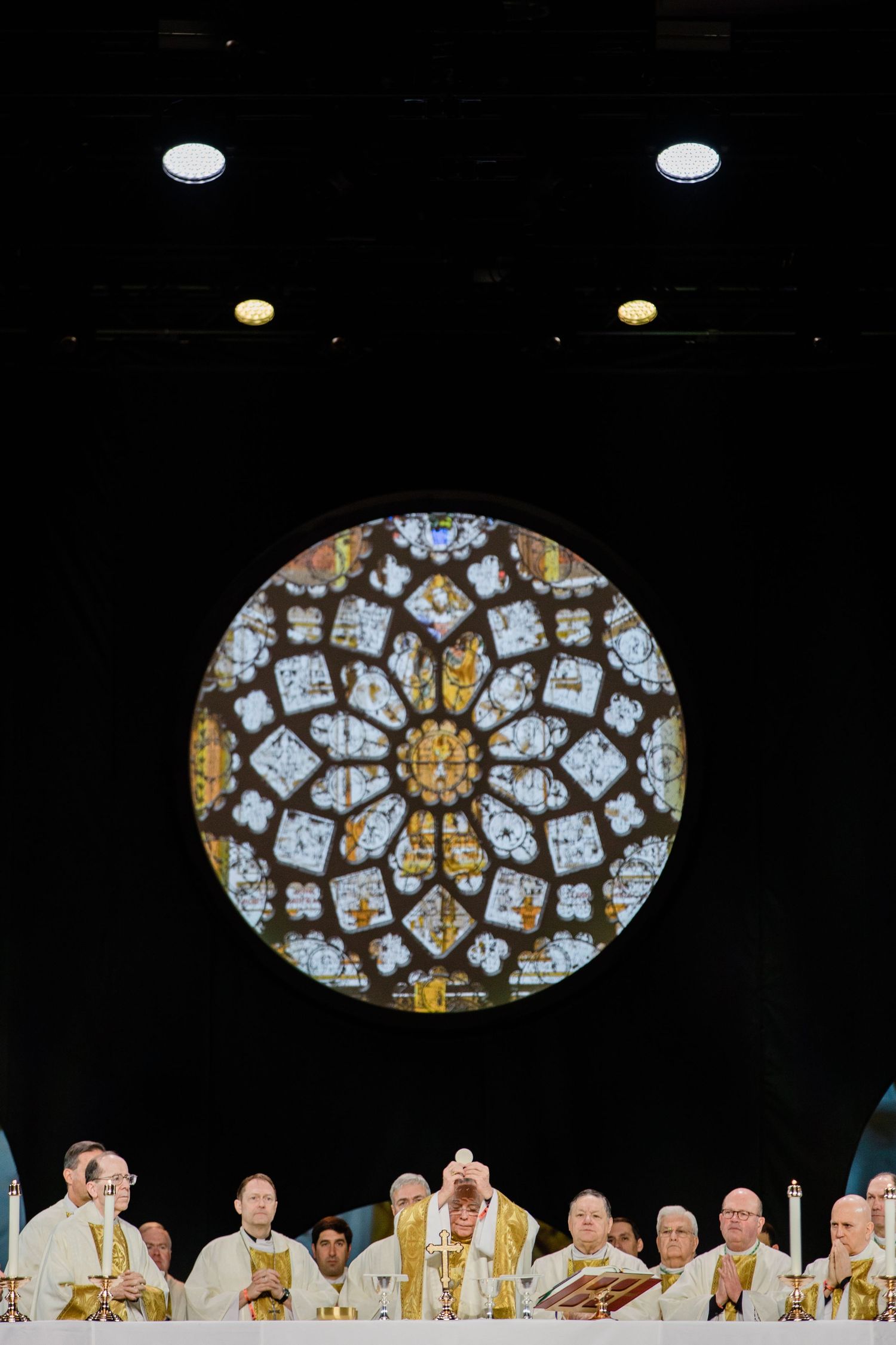 Ornate stained glass rose window above religious ceremony in cathedral.