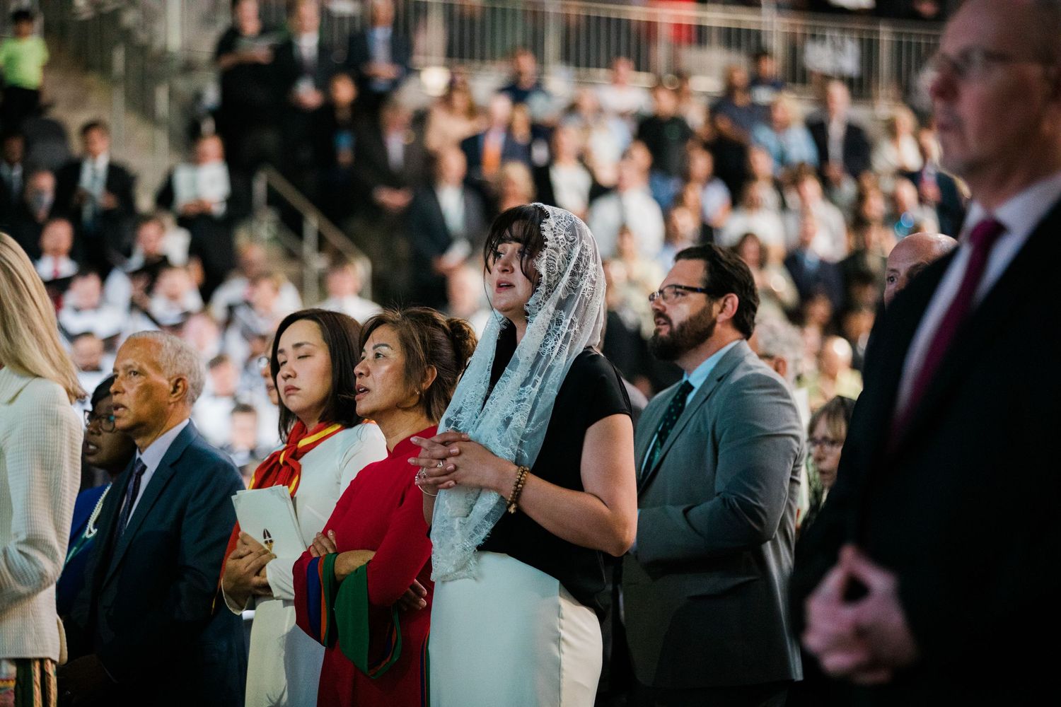Wedding guests stand together during an emotional ceremony moment at an indoor venue.