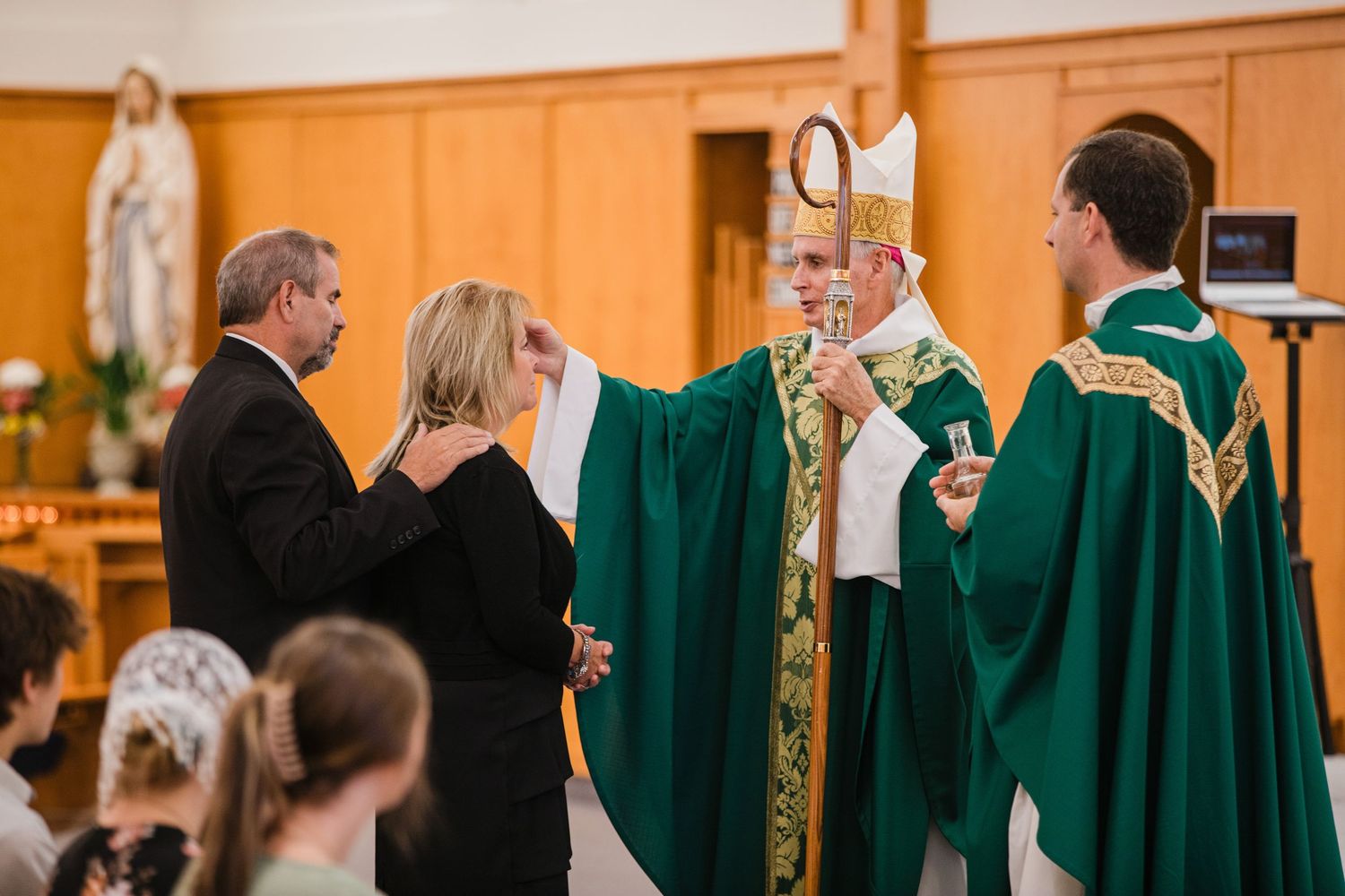 Religious ceremony in progress with clergy in green robes performing blessing ritual inside church sanctuary.
