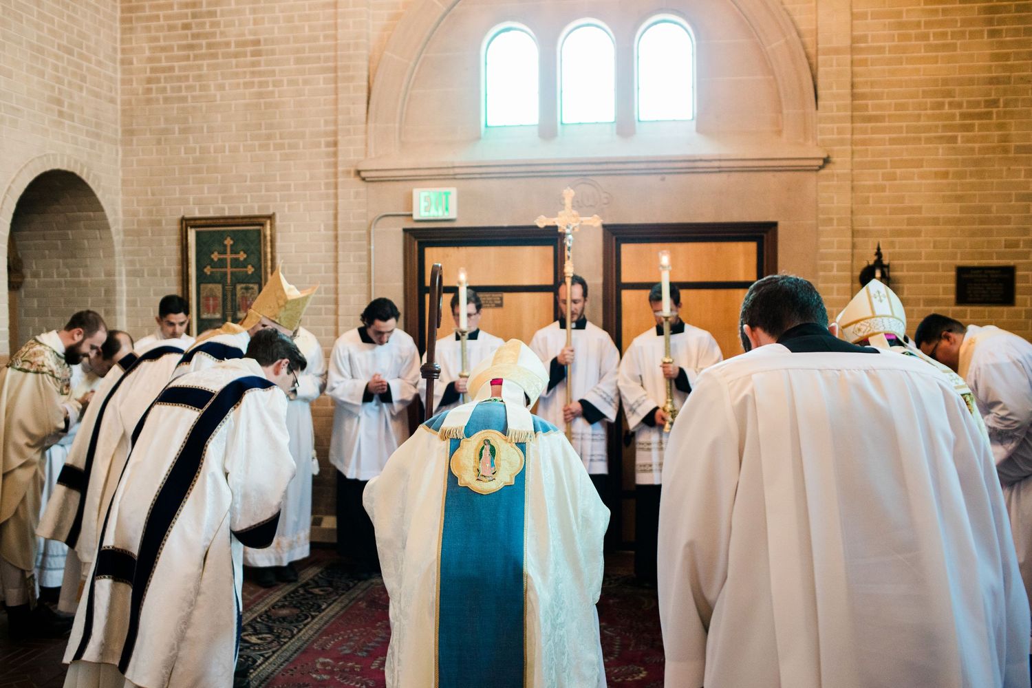 Catholic clergy in white robes participate in solemn religious ceremony inside a stone church.
